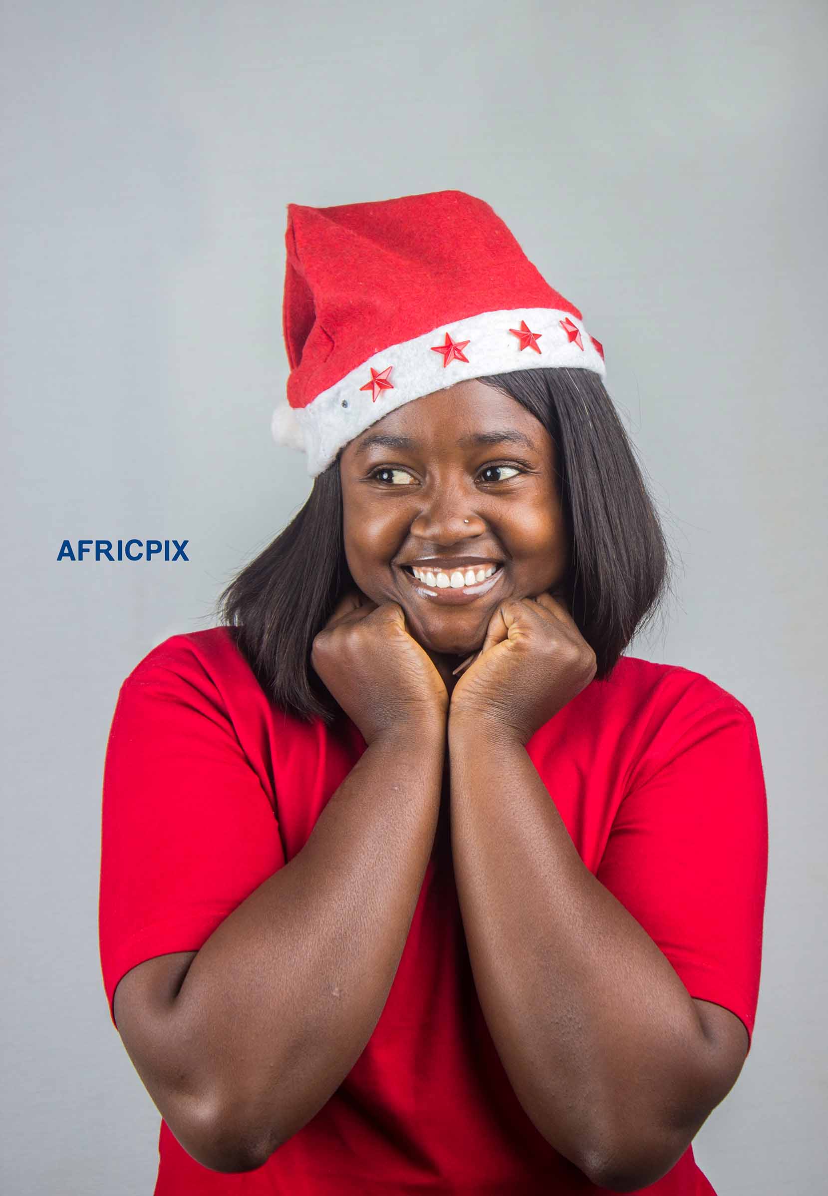 A happy African woman wearing a Christmas cap with her hands on her cheeks, smiling joyfully.